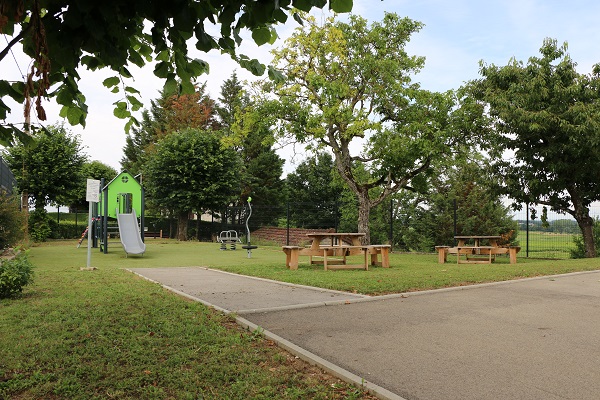 Un parc arboré avec ses jeux et des tables avec bancs